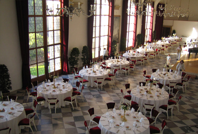 obszerna i wysoka sala z wysokimi oknami i ułożonymi okrągłymi stołami na uroczystość - dawna Sala do gry w piłkę w Ogrodach Królewskich w Pradze