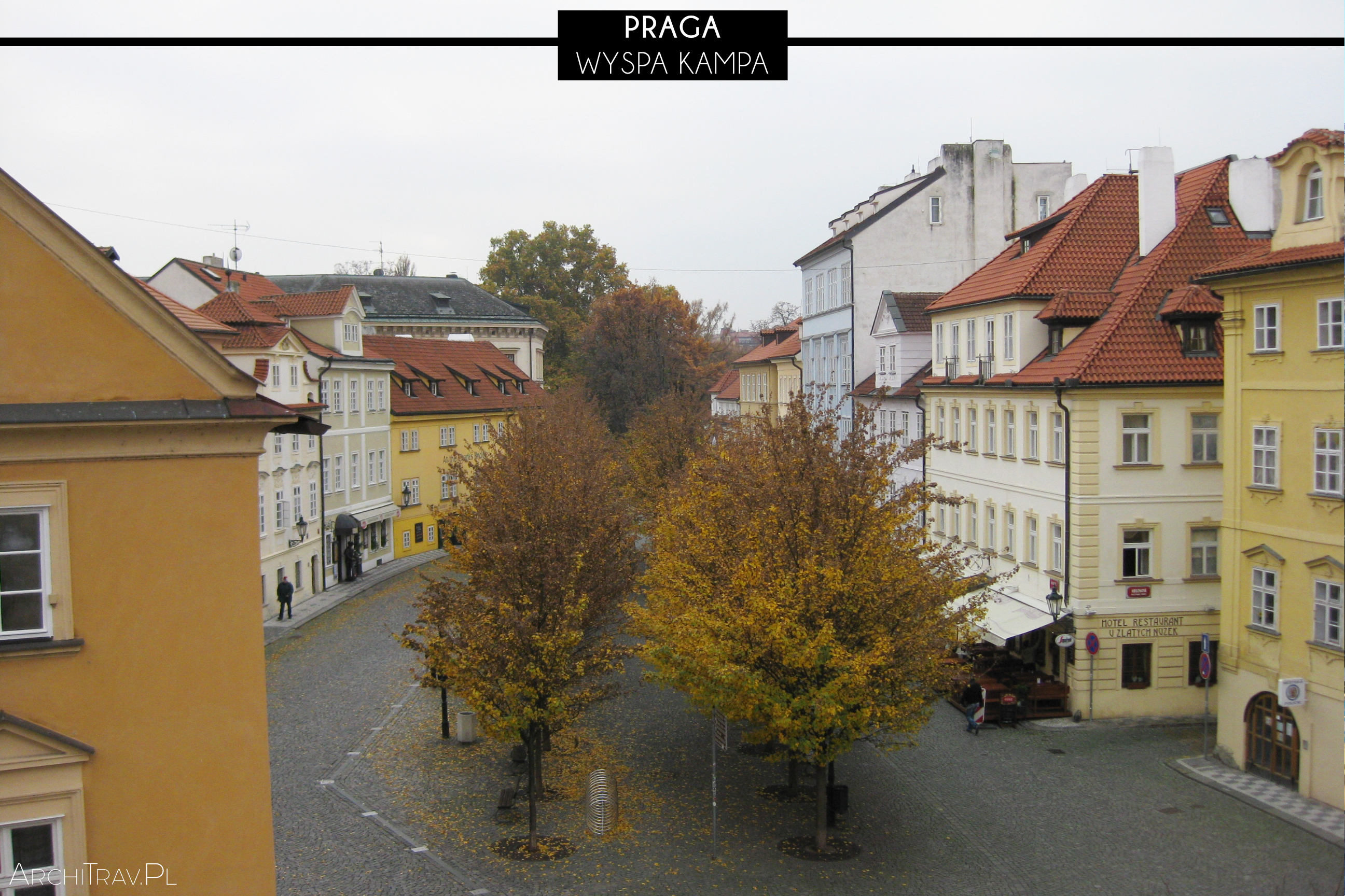 widok na wyspę z Mostu Karola, widzimy drzewa po środku placu, a wokół nich budynki, jest jesień